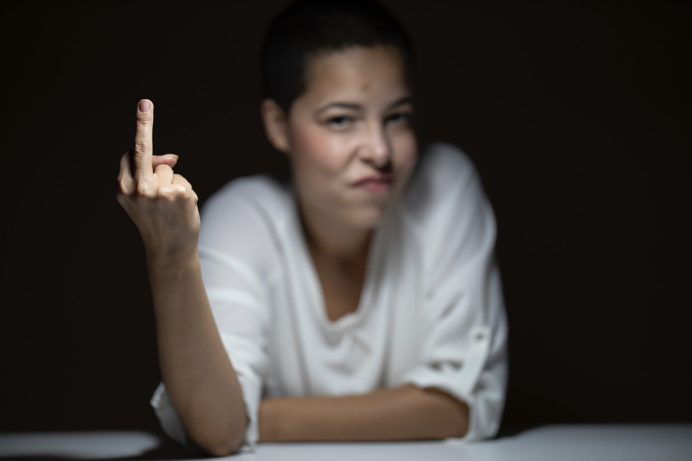 A woman in a white shirt sticks up her middle finger and sneers.
