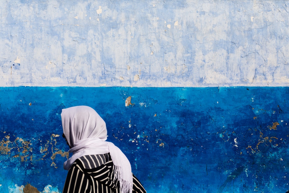 person wearing hijab walking in front of an aquamarine painted wall